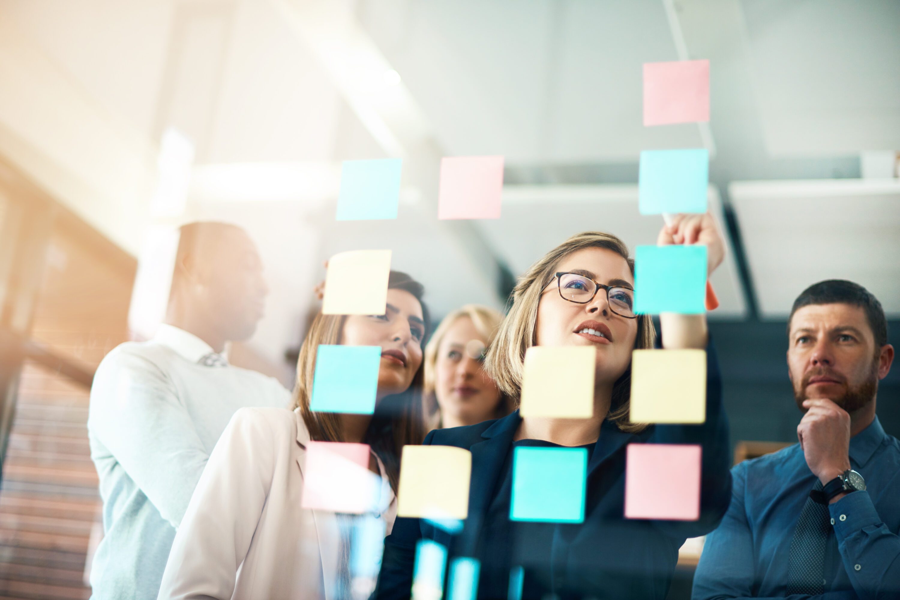 Colleagues look at sticky notes on a glass wall