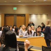 A group of young women sit inside a classroom and pay attention attentively to the speaker at the front of the room