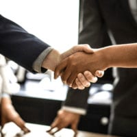 A business professional in a suit firmly shakes hands with another professional