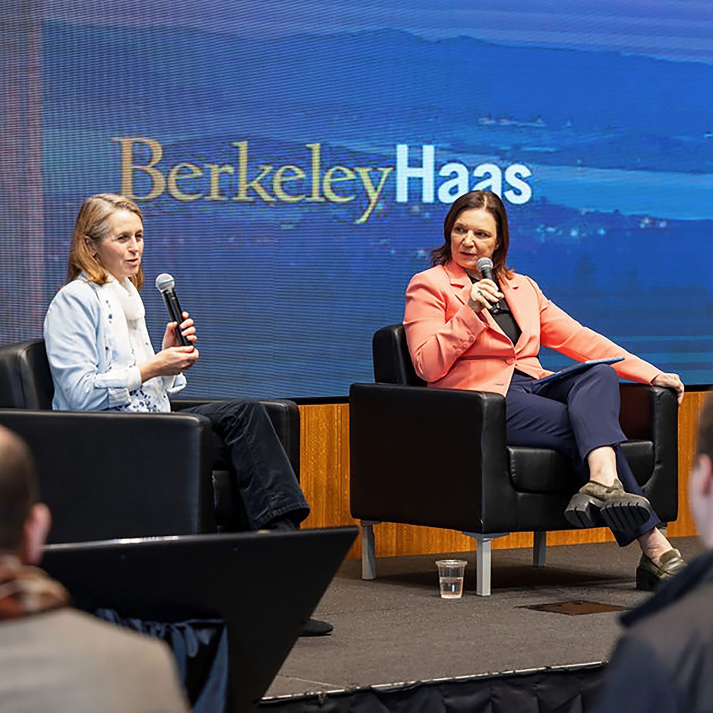 Dean Ann Harrison holds a microphone to interview Professor Catherine Wolfram on stage at Spieker Forum, Haas School of Business.