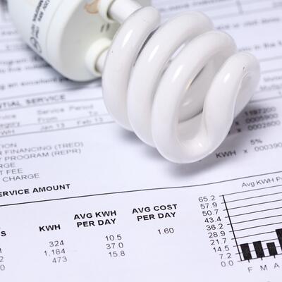 a white spiral compact fluorescent light bulb resting on an electricity bill.
