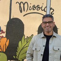 Richard Raya stands in front of a mural