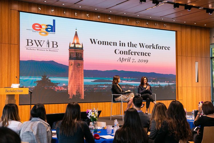 A conference stage with two women speaking at a “Women in the Workforce” event.