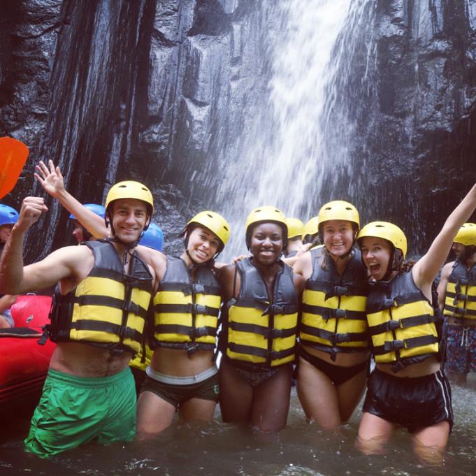 Group of people in life jackets in front of waterfall