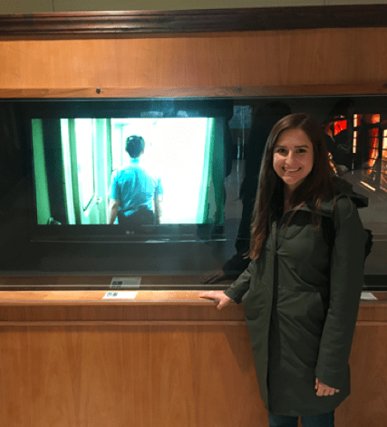 '19 MBA Rachel Green in front of Global Lives Project Video Exhibit